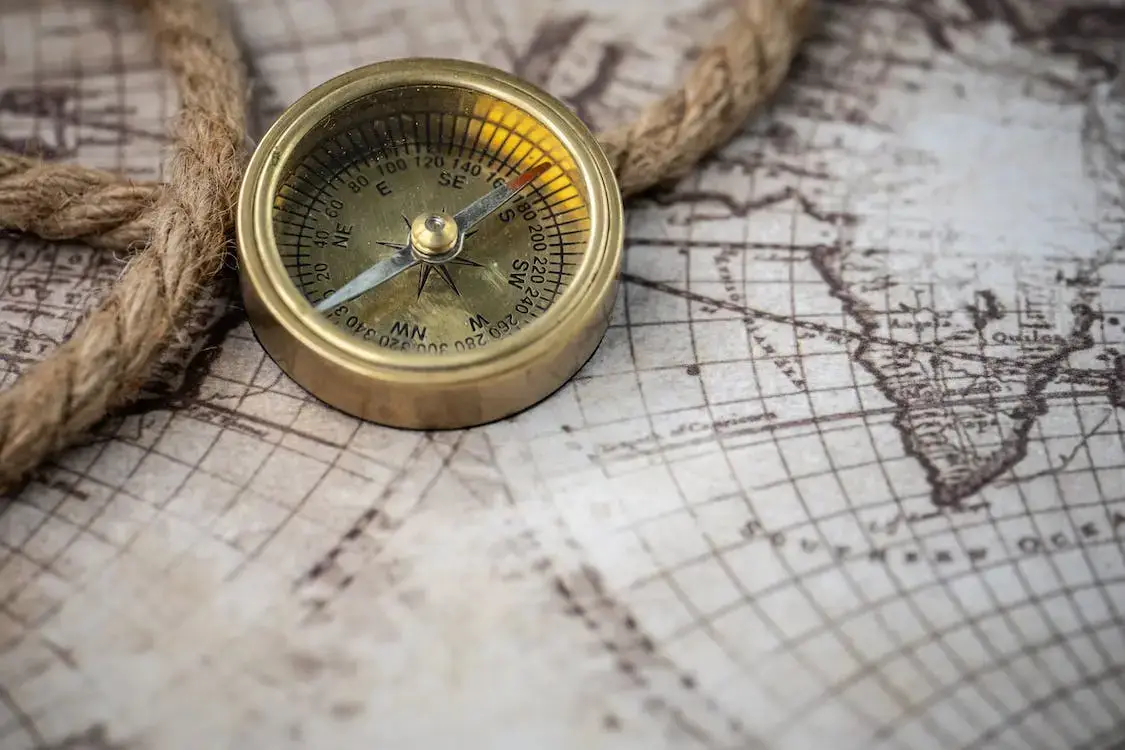 A brass compass rests on a vintage map alongside a coiled rope, suggesting themes of exploration and navigation. The map features detailed, old-fashioned lines and outlines of continents. STG-Health